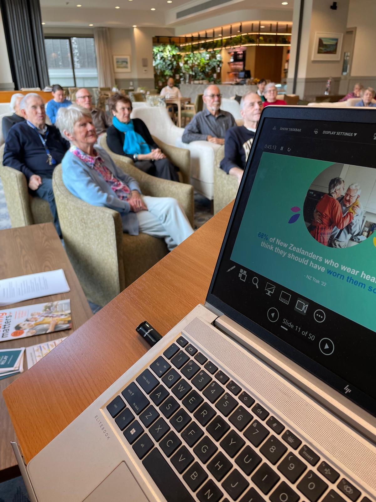 Laptop with the hearing health presentation with residents listening in the background